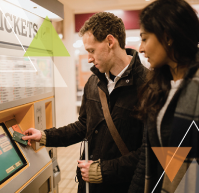 A man and woman stand at a ticket kiosk. The man is helping solve transit challenges for MTM Transit while ensuring every trip is important.