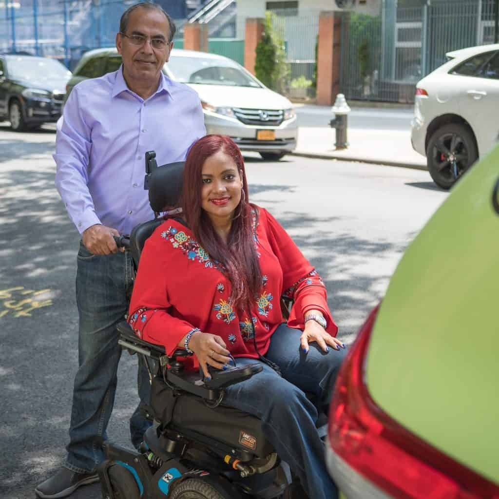 A driver stands behind a woman who utilizes a wheelchair. On behalf of the TLC's Accessible Dispatch program, MTM dispatches accessible taxis to New Yorkers with disabilities.