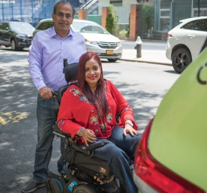 A driver stands behind a woman who utilizes a wheelchair. On behalf of the TLC's Accessible Dispatch program, MTM dispatches accessible taxis to New Yorkers with disabilities.
