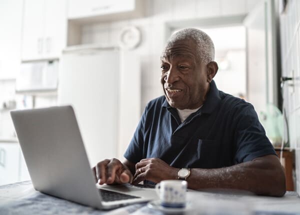 An older man sits behind his laptop using Mobility Direct, MTM Transit's online paratransit eligibility software that uses our remote ADA certification process.