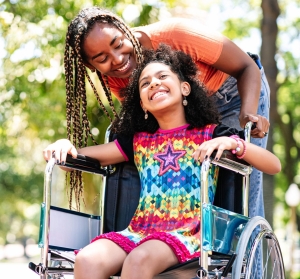 Little girl in a wheelchair at the park with her mother.