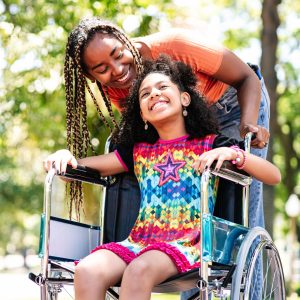 Little girl in a wheelchair at the park with her mother.