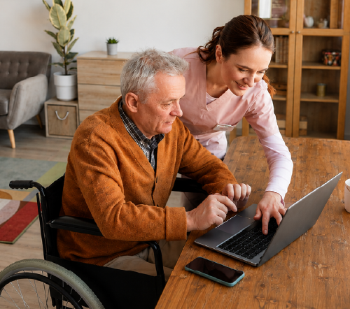 Caretaker helping senior man in a wheelchair with his computer